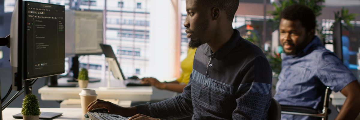 Programmer doing software debugging, asking for help from smiling team leader in wheelchair. Employee fixing coding mistakes, being assisted by cheerful manager with disability, camera A